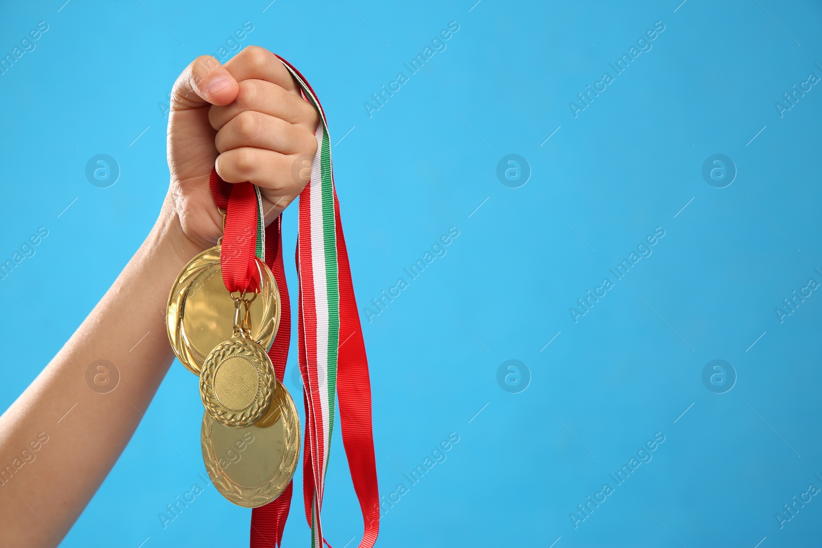 Photo of Woman holding gold medals on light blue background, closeup. Space for text