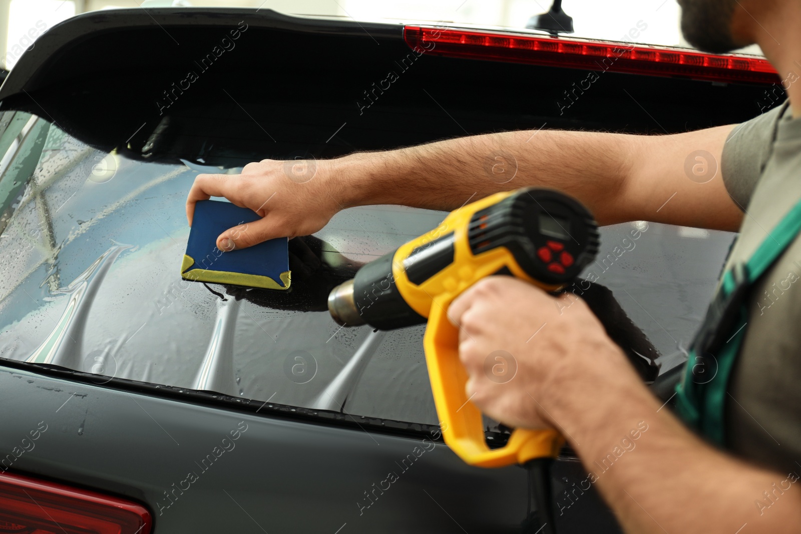 Photo of Worker tinting car window with heat gun in workshop, closeup