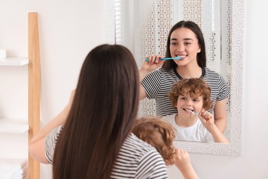 Mother and her son brushing teeth together near mirror in bathroom