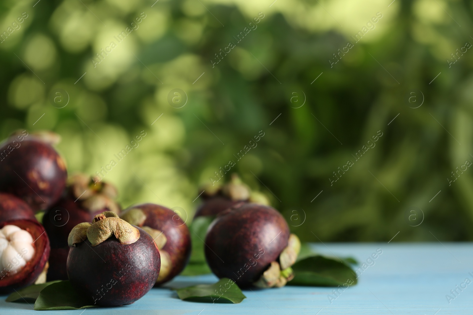 Photo of Delicious tropical mangosteen fruits on light blue table. Space for text