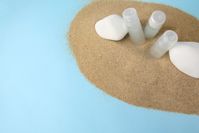 Bottles of serum and stones on sand against light blue background, above view with space for text. Cosmetic product