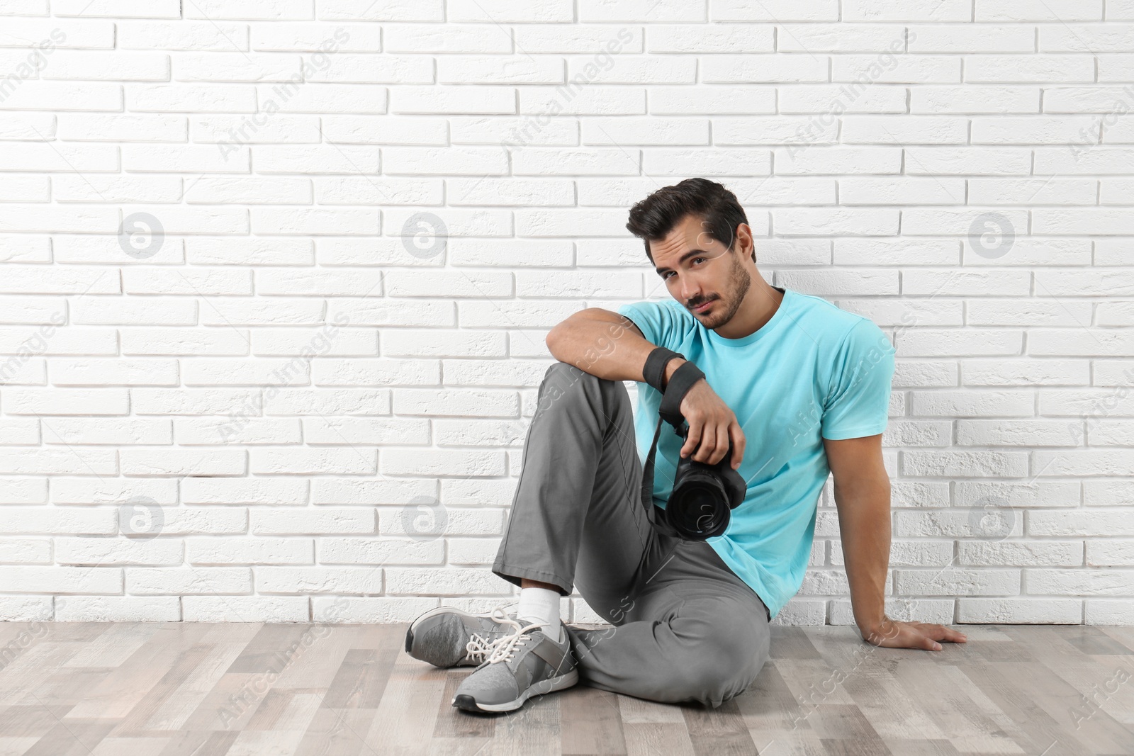 Photo of Young photographer with professional camera near brick wall. Space for text