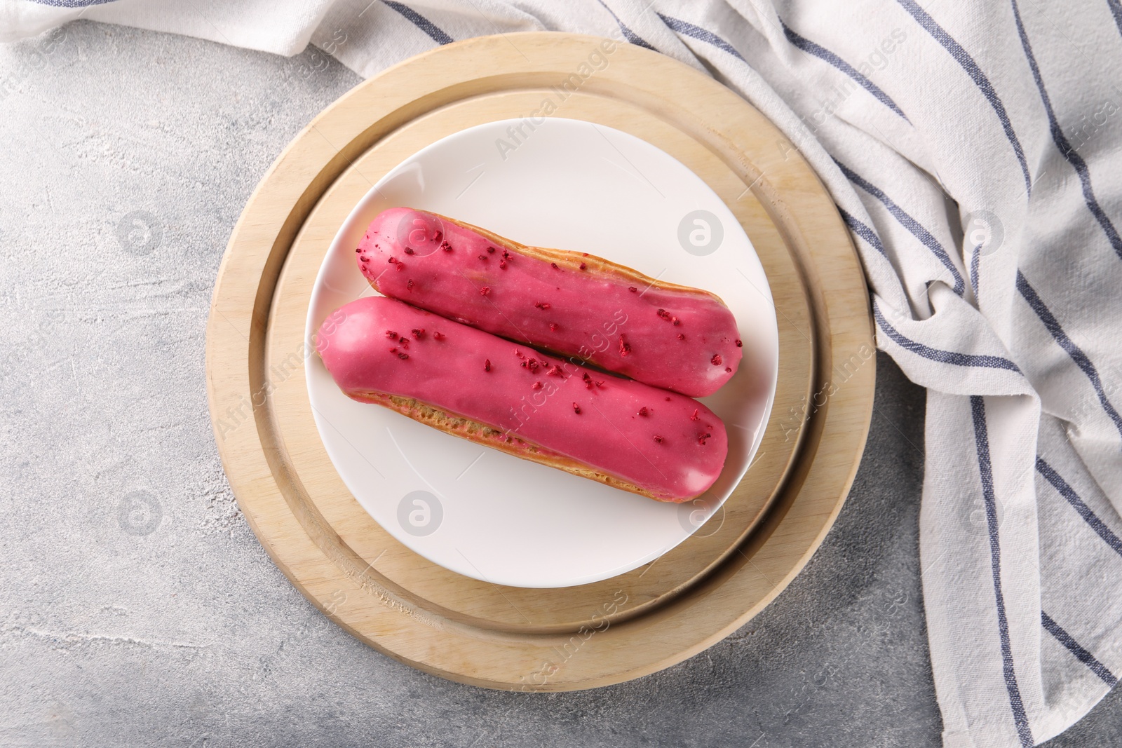 Photo of Plate with tasty glazed eclairs on grey textured table, top view