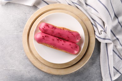 Plate with tasty glazed eclairs on grey textured table, top view