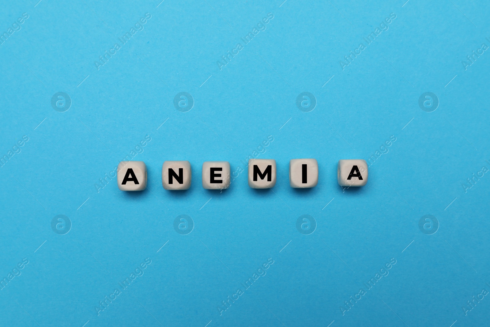 Photo of Word Anemia made of small wooden cubes on light blue background, flat lay
