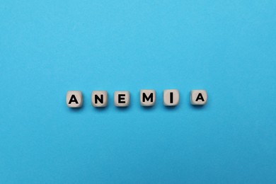 Word Anemia made of small wooden cubes on light blue background, flat lay