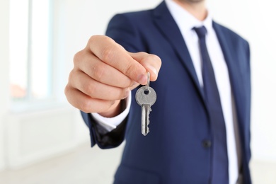 Real estate agent holding key on blurred background, closeup