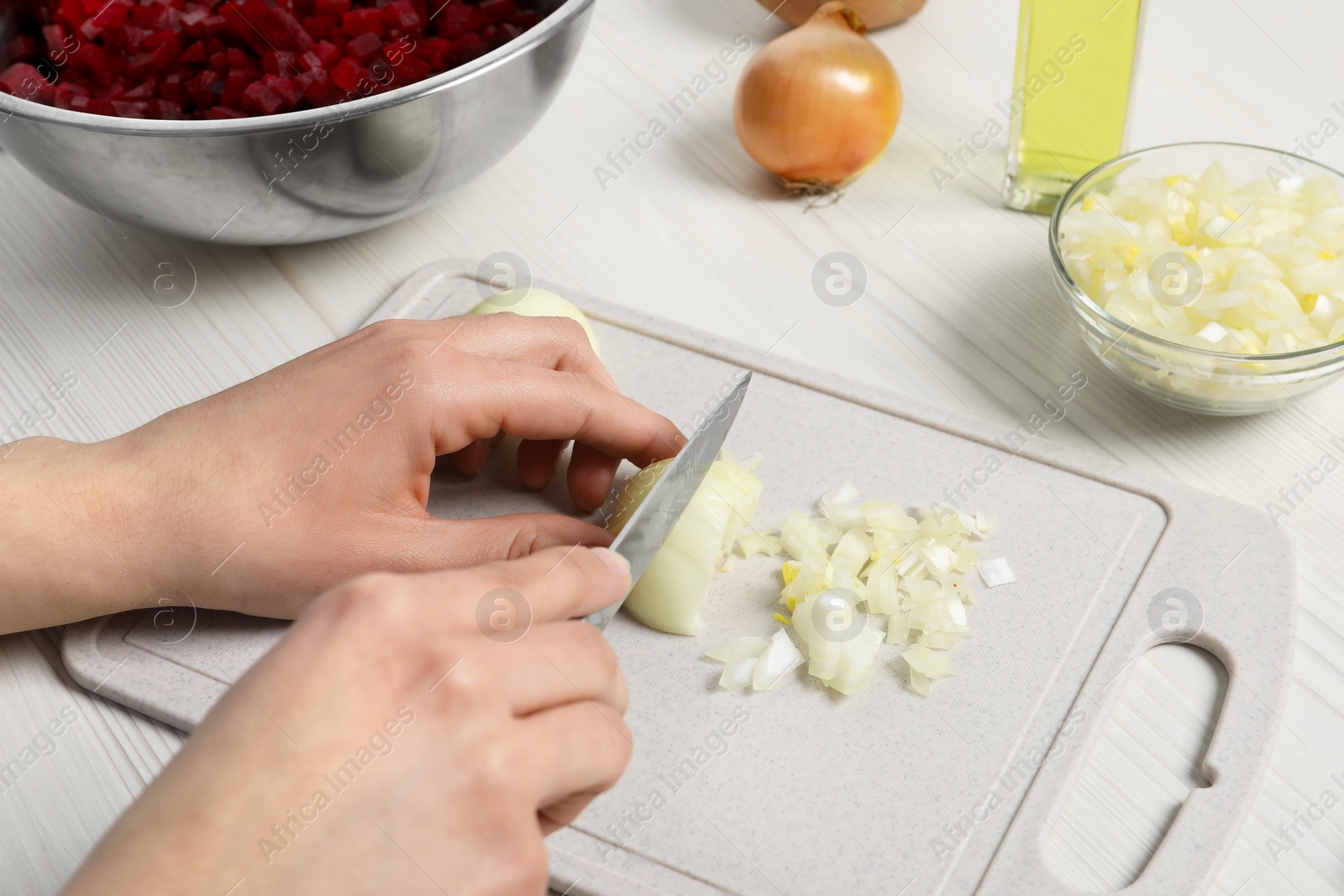 Photo of Woman cutting onion at white wooden table, closeup. Cooking vinaigrette salad