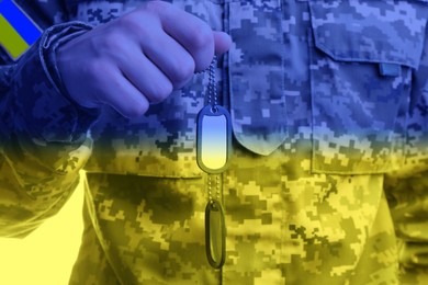 Image of Closeup view of defender in camouflage uniform holding military ID tags, toned in colors of Ukrainian flag