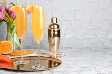 Glasses of Mimosa cocktail with garnish on white marble table. Space for text