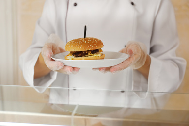 Photo of School canteen worker with burger at serving line, closeup. Tasty food
