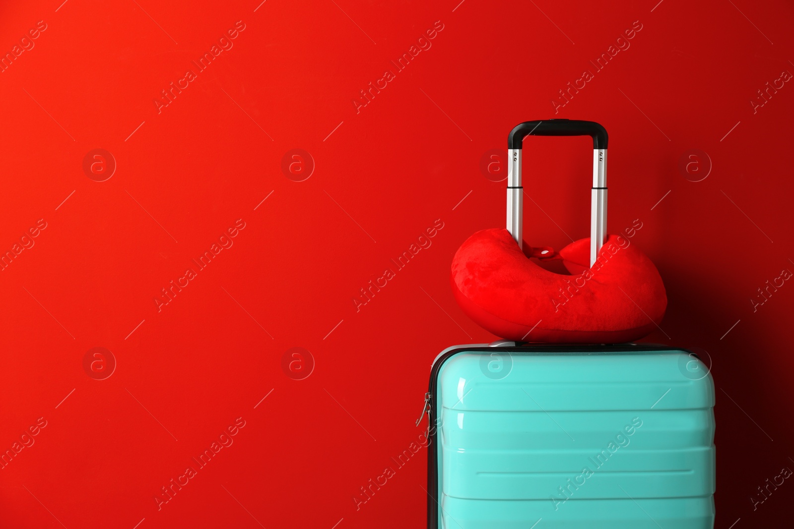 Photo of Turquoise suitcase and travel pillow on red background, space for text