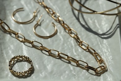 Metal chain and other different accessories on white dish, closeup. Luxury jewelry