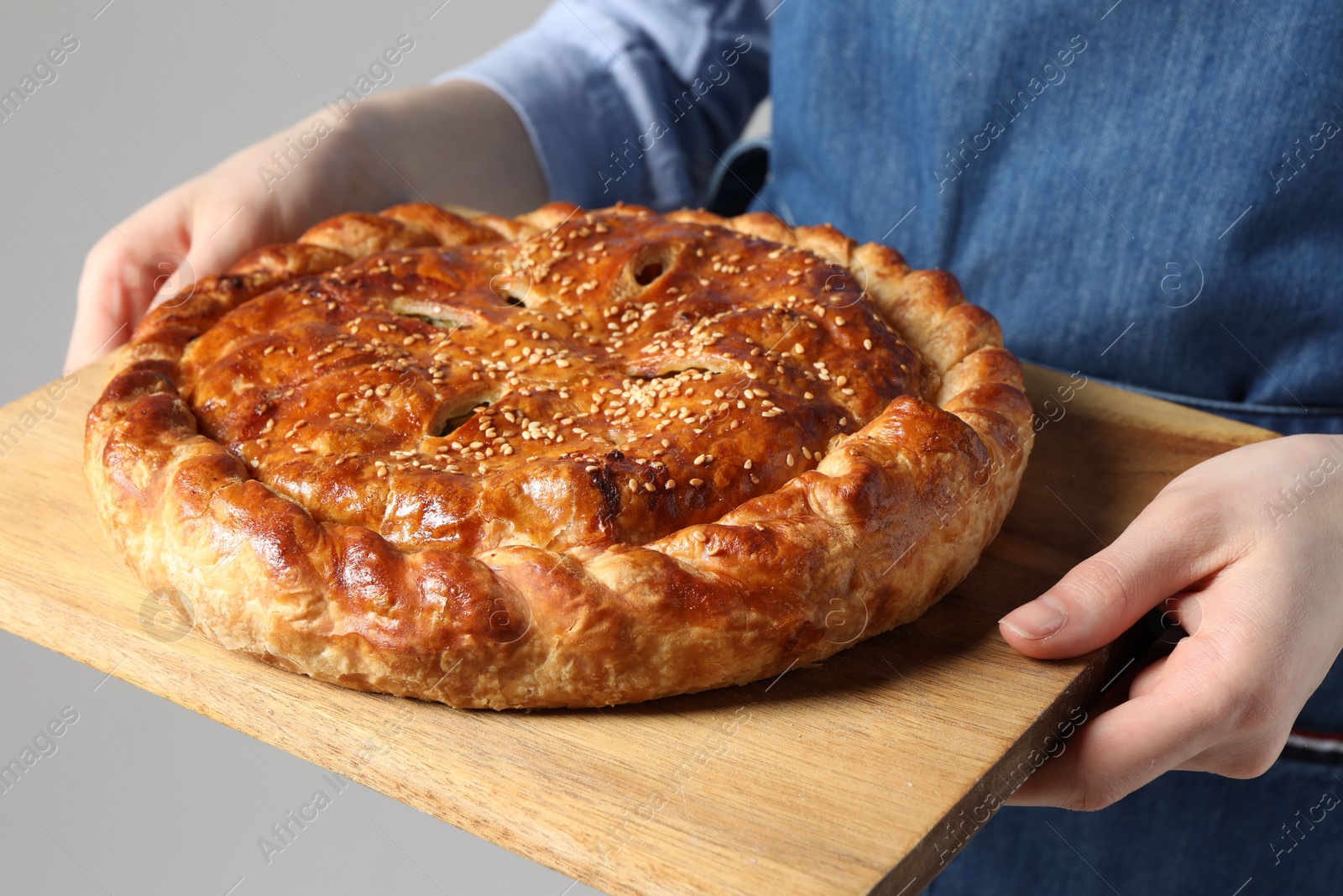 Photo of Woman holding tasty homemade pie on light grey background, closeup