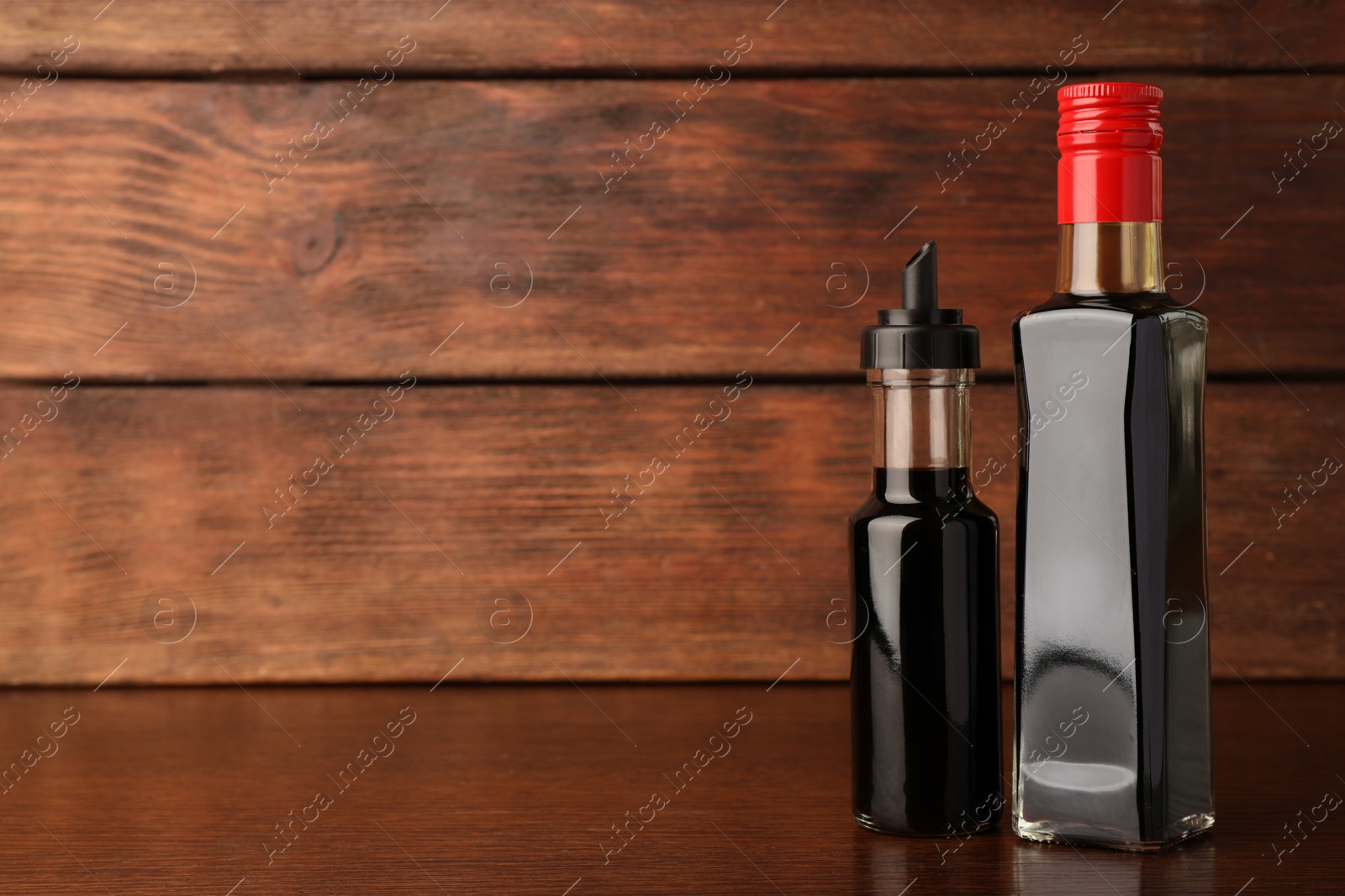 Photo of Bottles with soy sauce on wooden table. Space for text