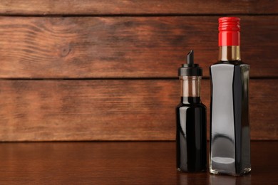 Photo of Bottles with soy sauce on wooden table. Space for text