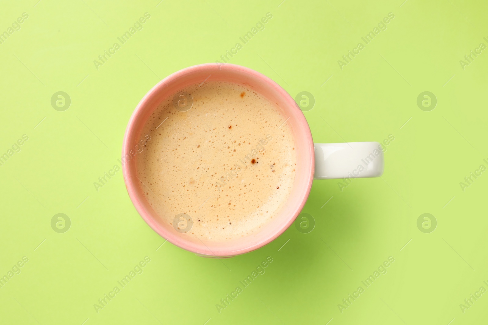 Photo of Aromatic coffee in cup on light green background, top view