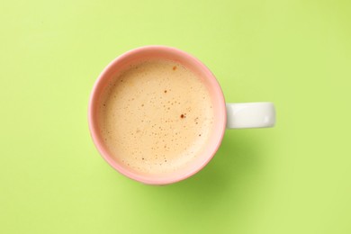 Aromatic coffee in cup on light green background, top view