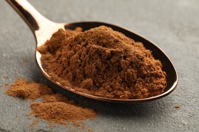 Photo of Spoon with cinnamon powder on grey table, closeup