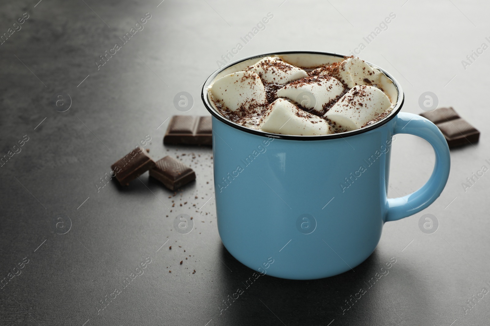 Photo of Delicious hot chocolate with marshmallows and cocoa powder in mug on grey table, space for text