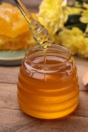 Photo of Pouring sweet golden honey from dipper into jar at wooden table, closeup