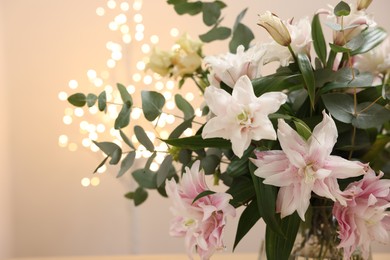 Photo of Bouquet of beautiful lily flowers against beige background with blurred lights, closeup