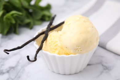 Photo of Delicious ice cream and vanilla pods on white marble table, closeup