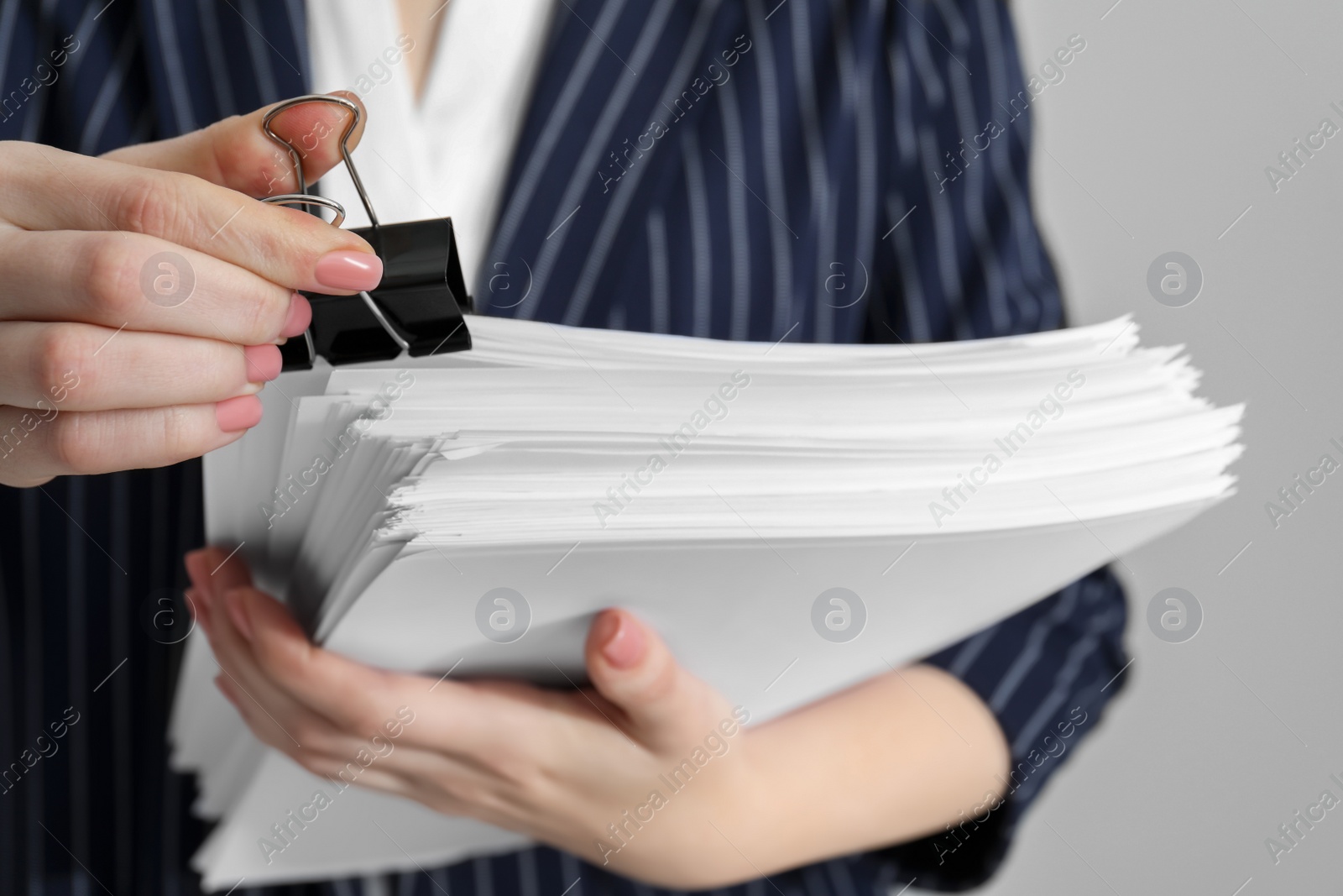 Photo of Woman attaching documents with metal binder clip on grey background, closeup