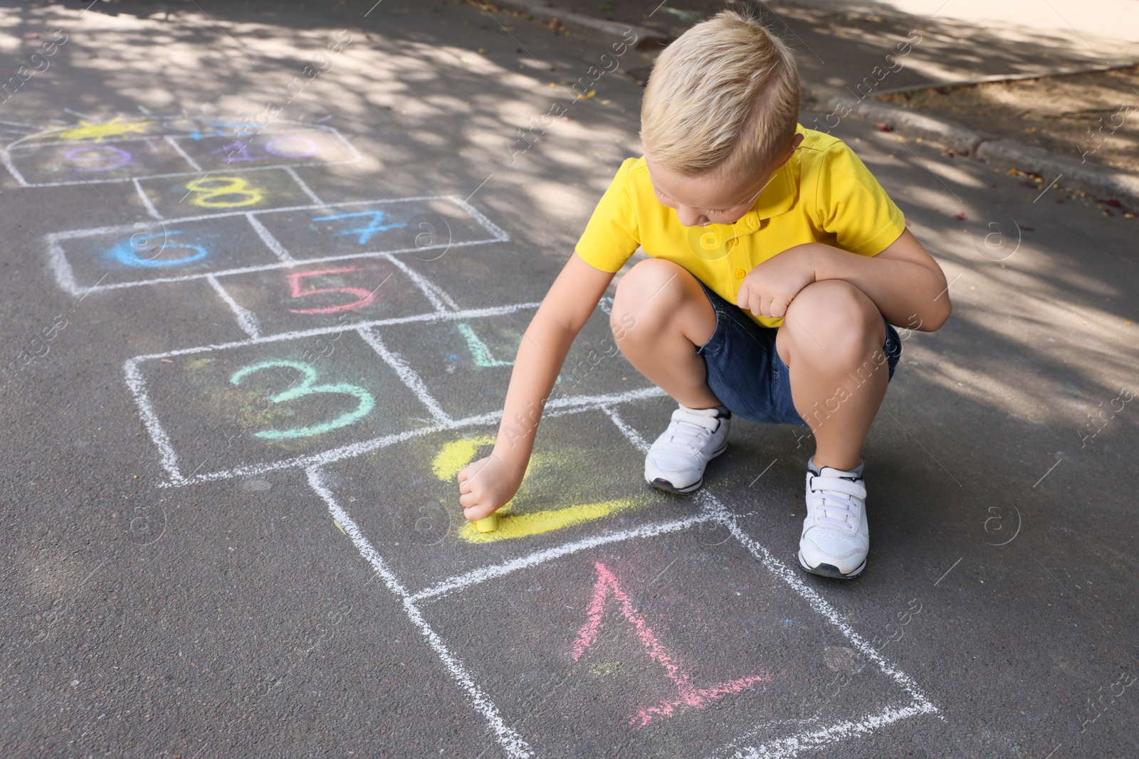Photo of Little boy drawing hopscotch with chalk on asphalt outdoors. Happy childhood