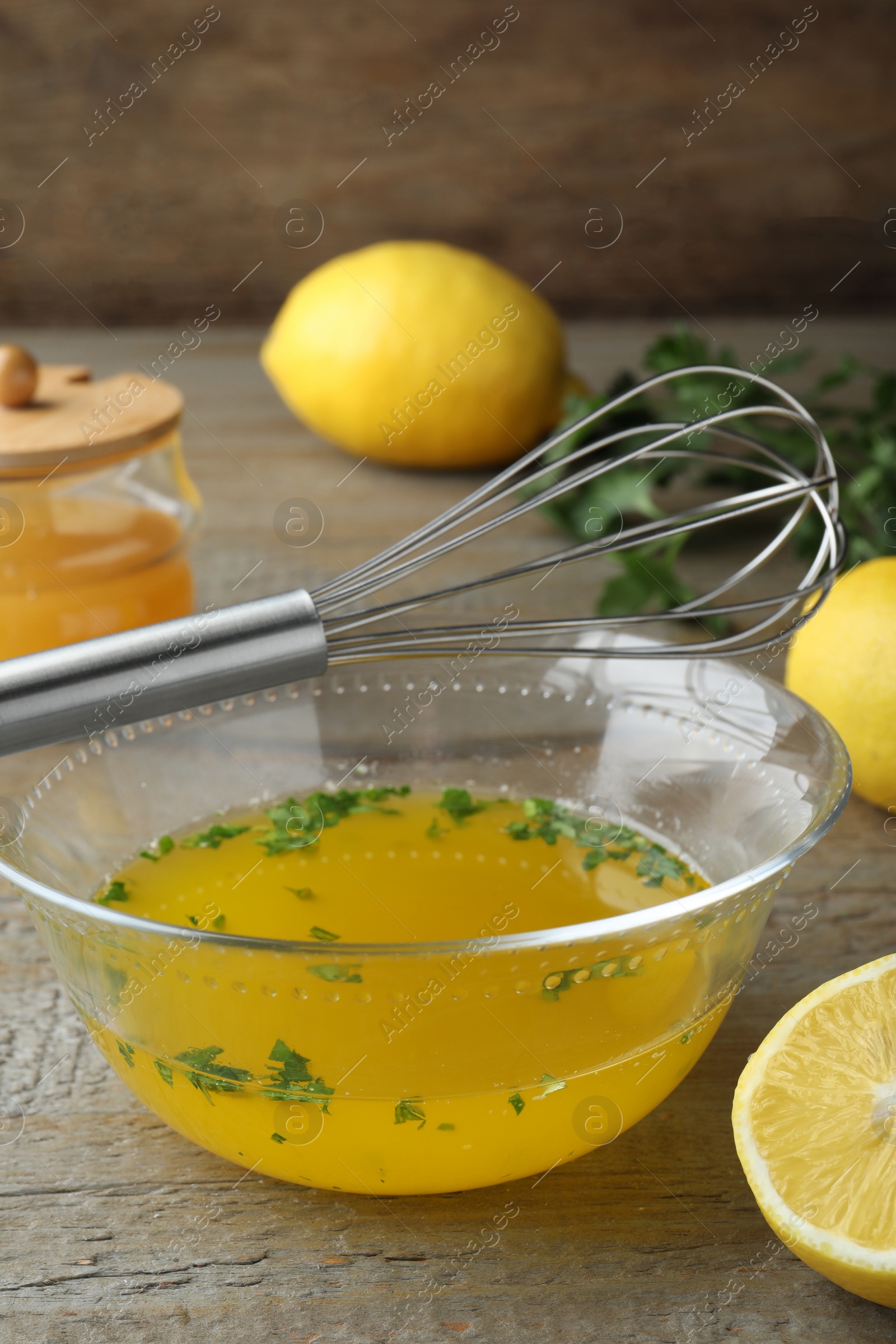 Photo of Whisk and bowl with lemon sauce on wooden table. Delicious salad dressing