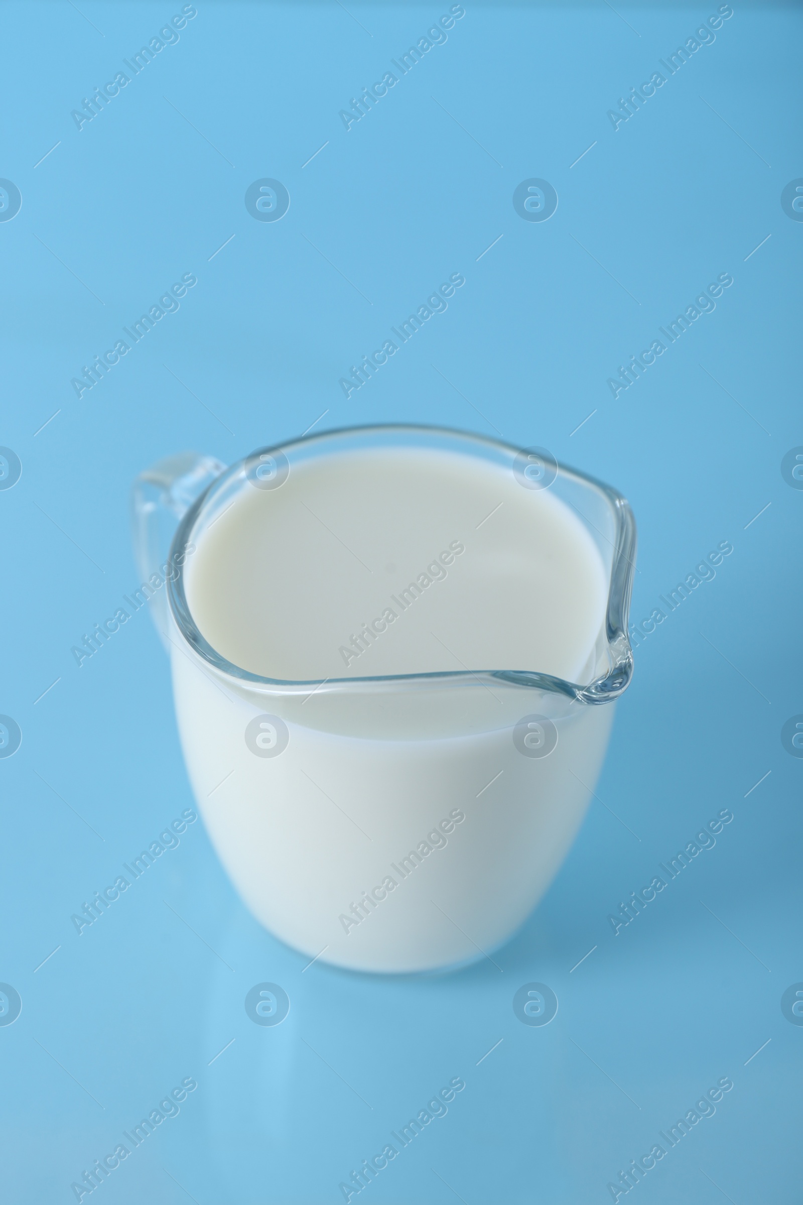 Photo of Jug of fresh milk on light blue background