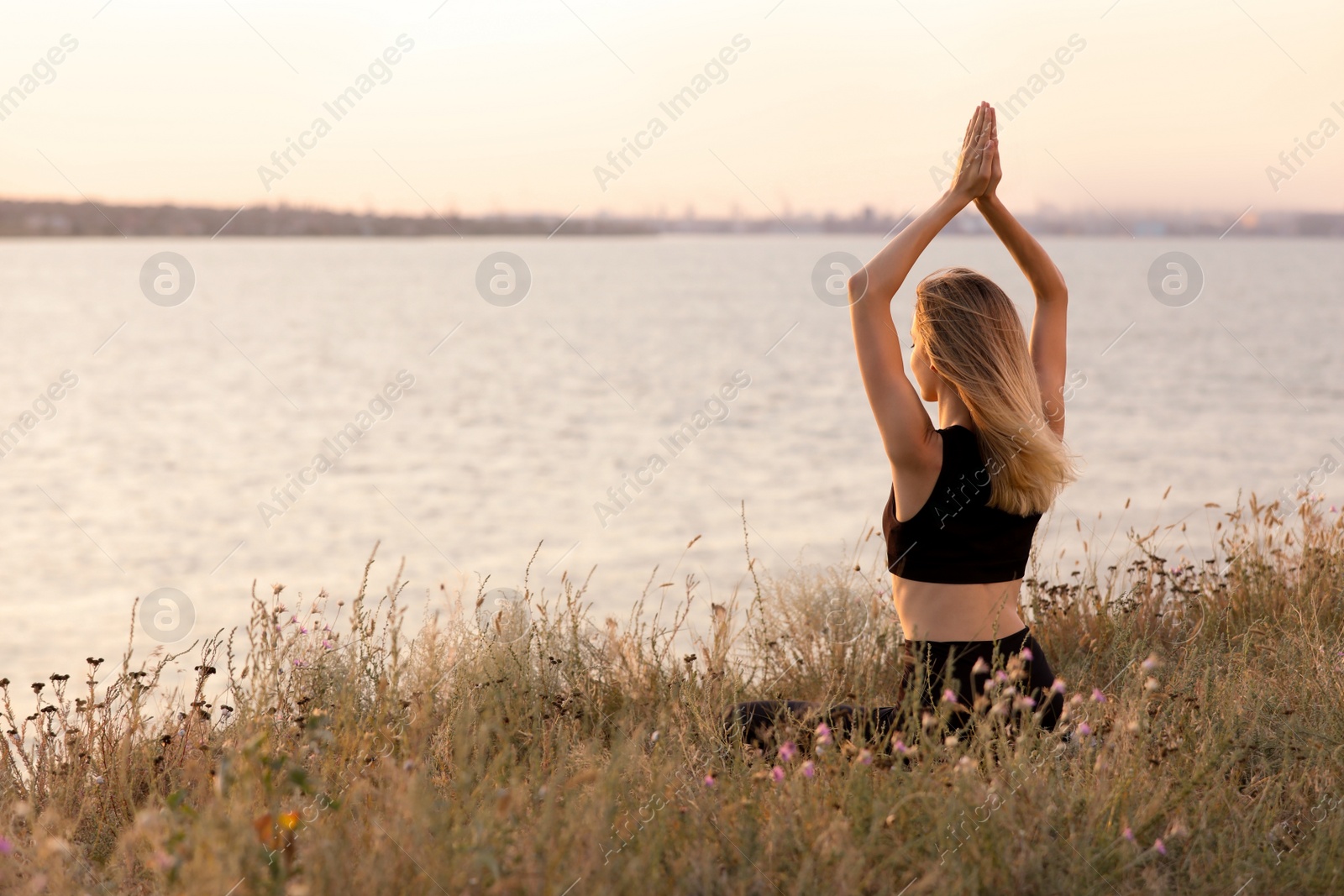 Photo of Young woman meditating near river on sunny day, back view. Space for text