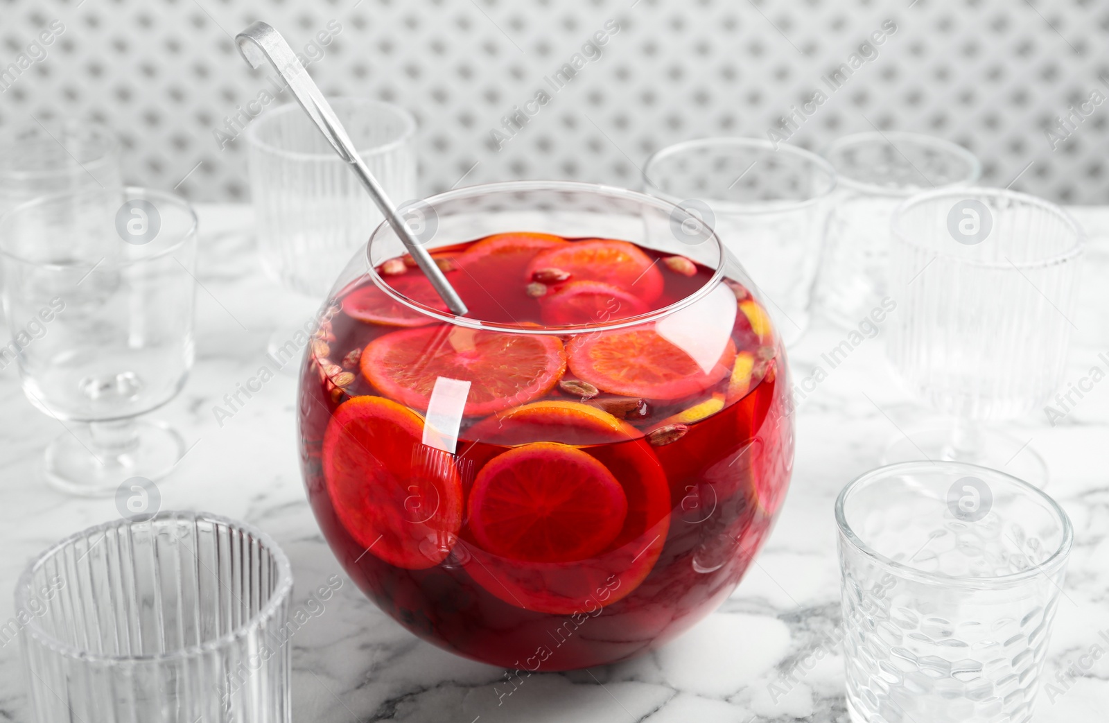 Photo of Bowl of delicious aromatic punch drink, ladle and empty glasses on white marble table