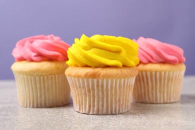 Photo of Delicious cupcakes with bright cream on gray table against violet background