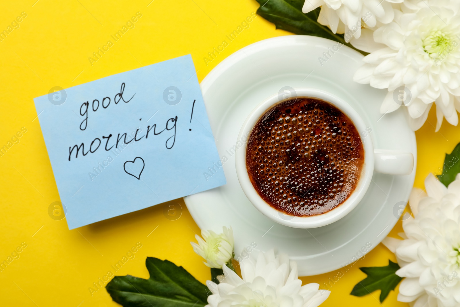 Photo of Cup of aromatic coffee, beautiful white chrysanthemums and Good Morning note on yellow background, flat lay