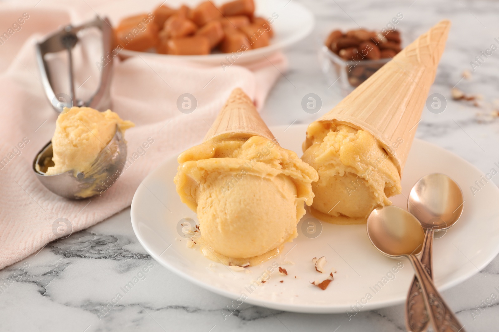 Photo of Plate with delicious yellow ice cream in wafer cones and spoons on white marble table, closeup