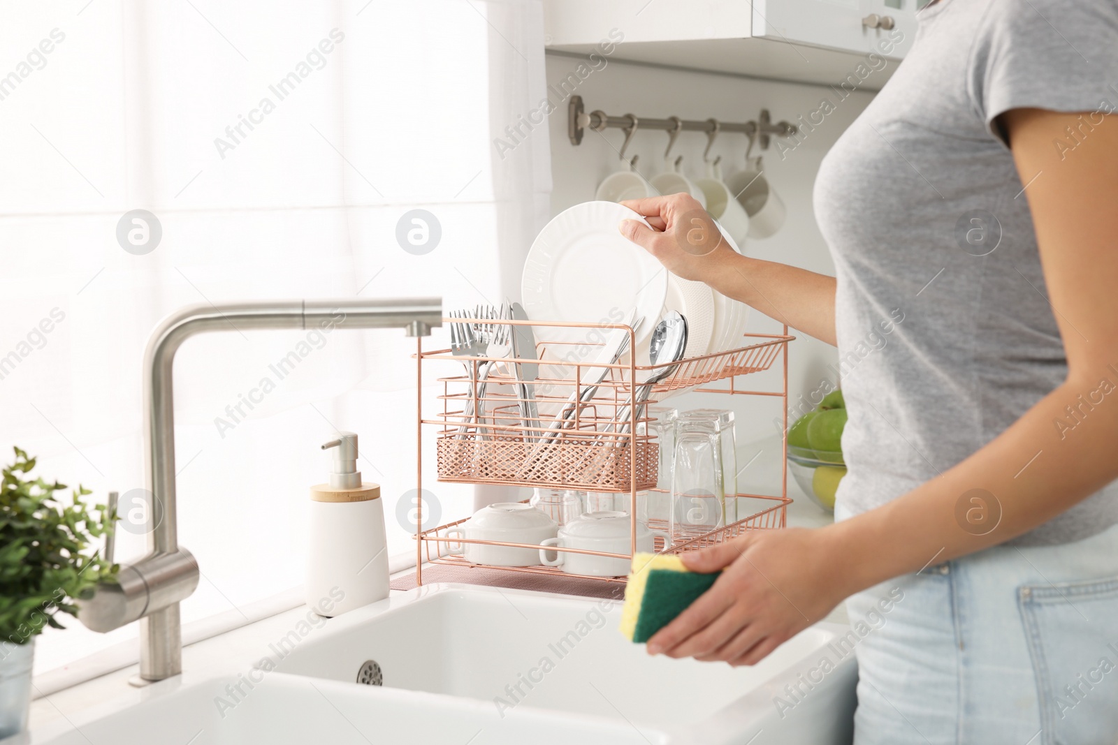 Photo of Woman putting clean dishes on drying rack in kitchen, closeup