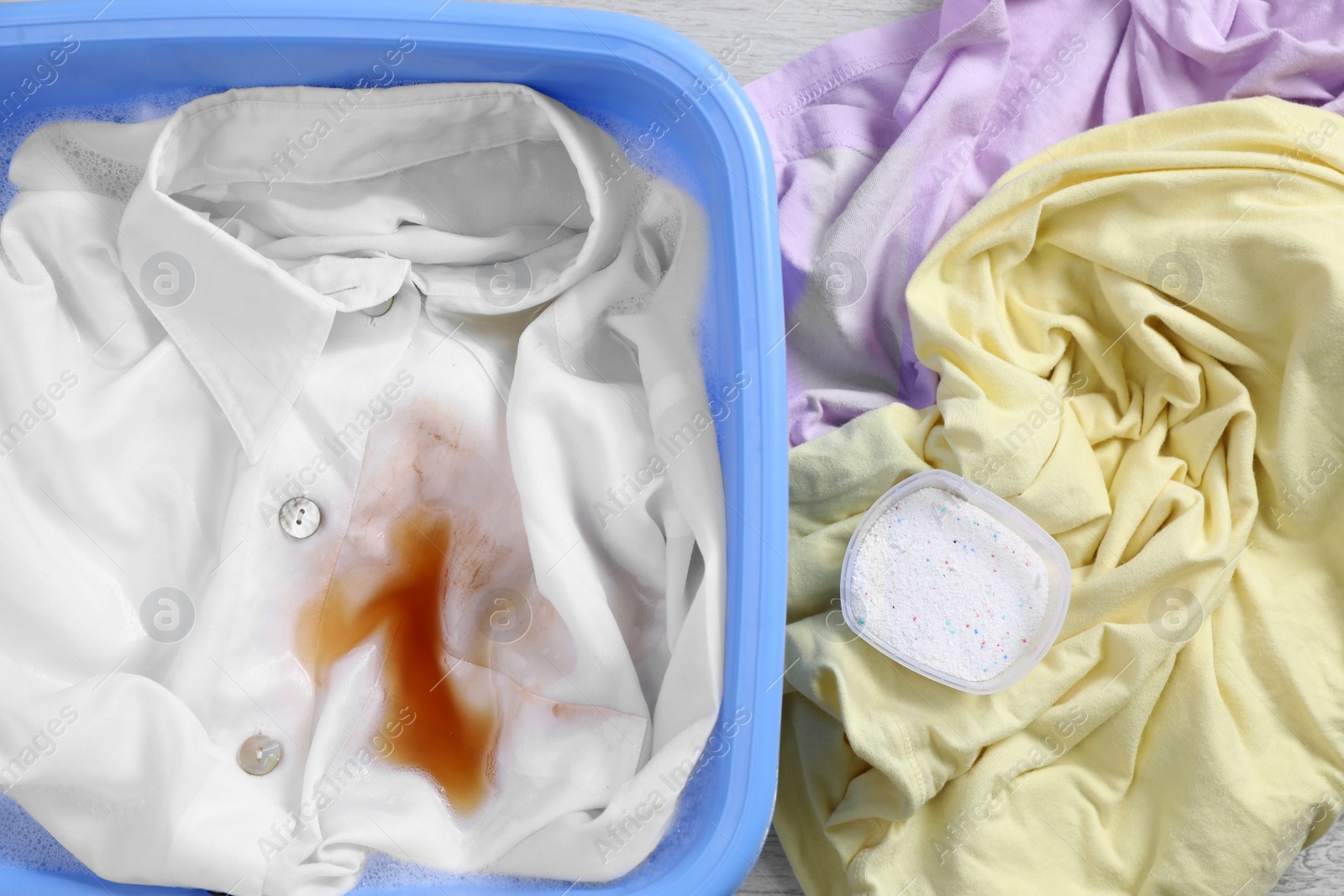 Photo of Garment and powdered detergent near basin with white shirt, top view. Hand washing laundry