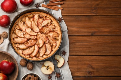 Photo of Delicious apple pie and ingredients on wooden table, flat lay. Space for text