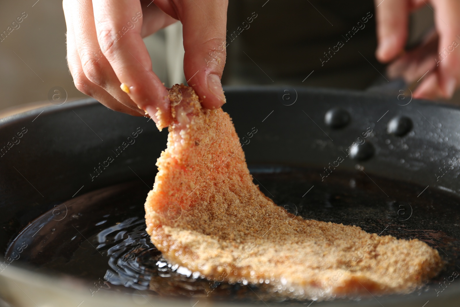 Photo of Cooking schnitzel. Woman putting raw pork chop in bread crumbs into frying pan, closeup