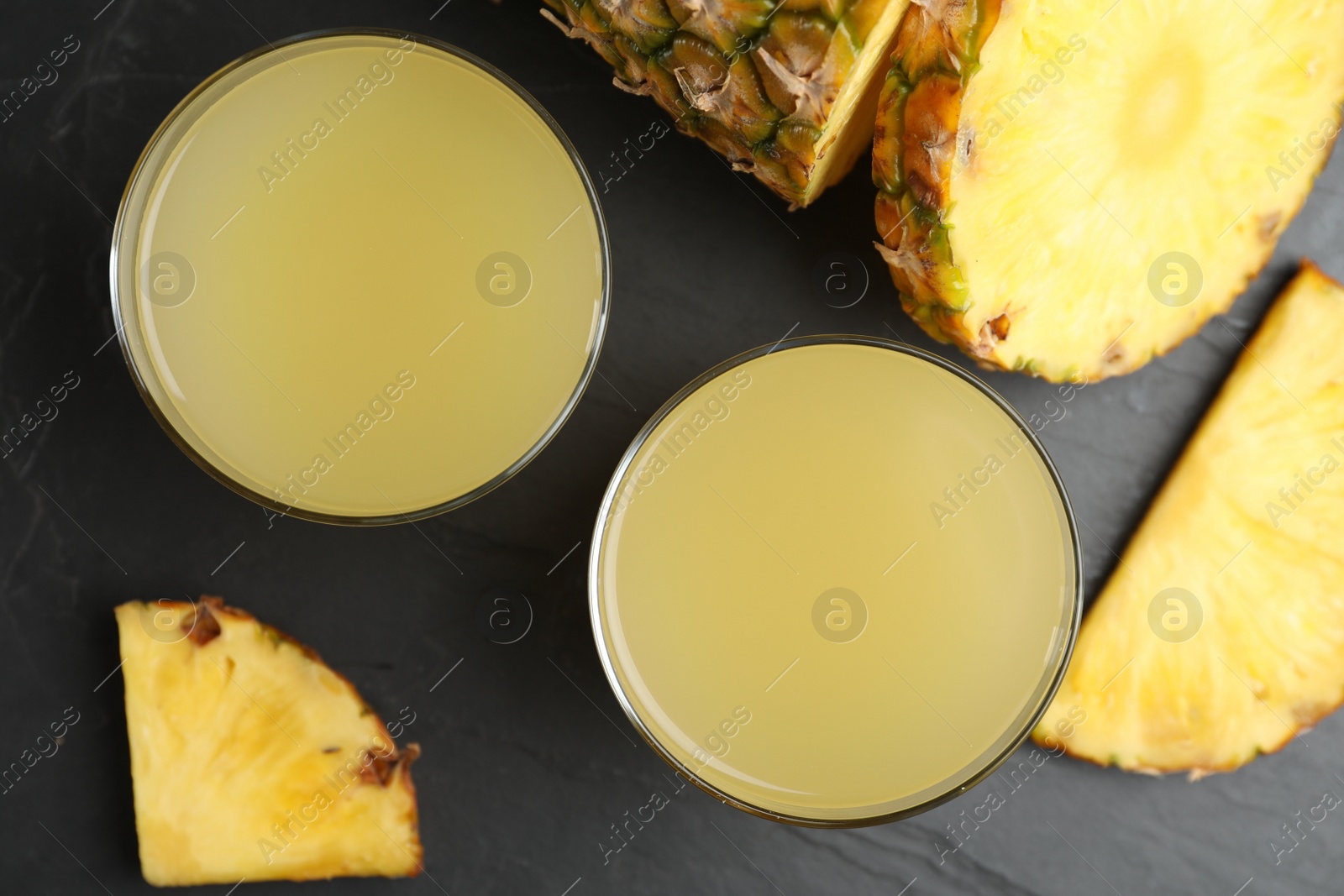 Photo of Delicious pineapple juice and fresh fruit on black table, flat lay