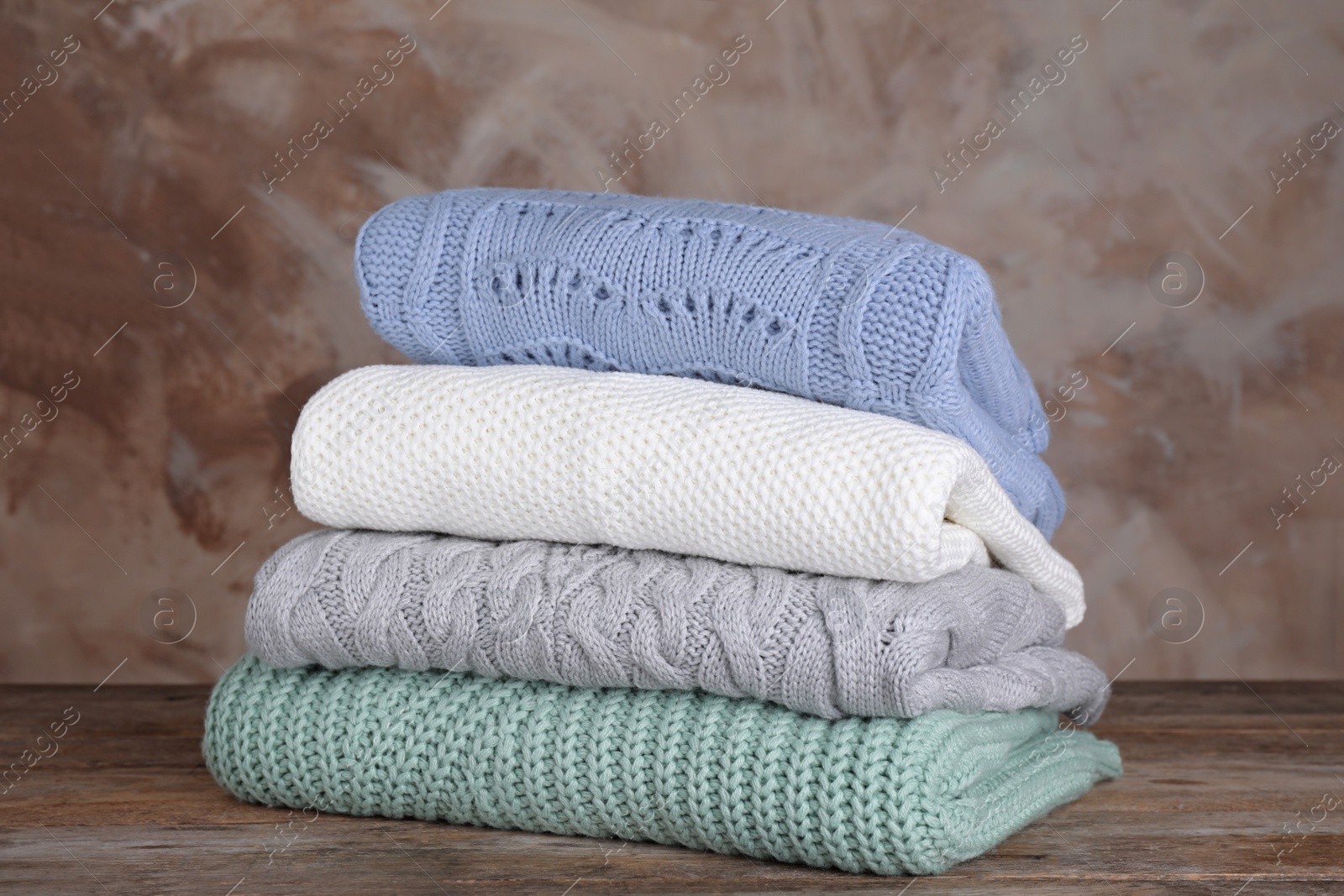 Photo of Stack of folded knitted sweaters on wooden table against brown background