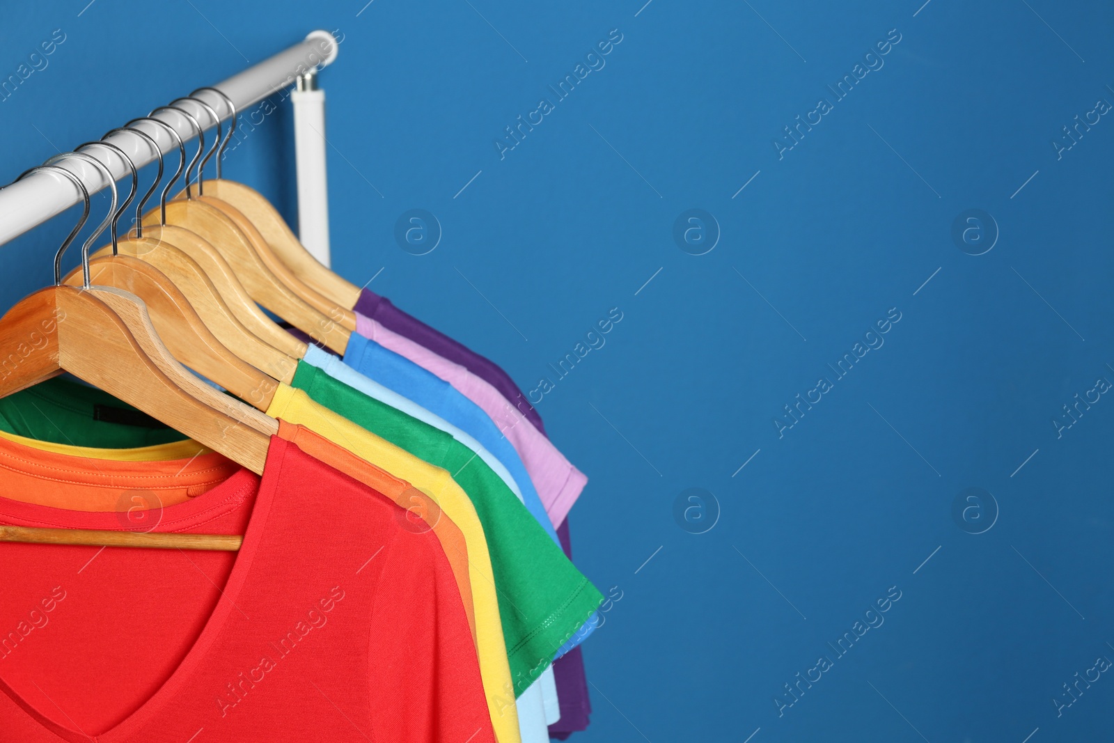 Photo of Bright clothes on blue background, space for text. Rainbow colors