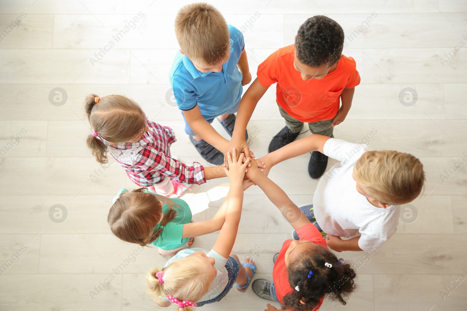 Photo of Little children putting their hands together indoors, top view. Unity concept