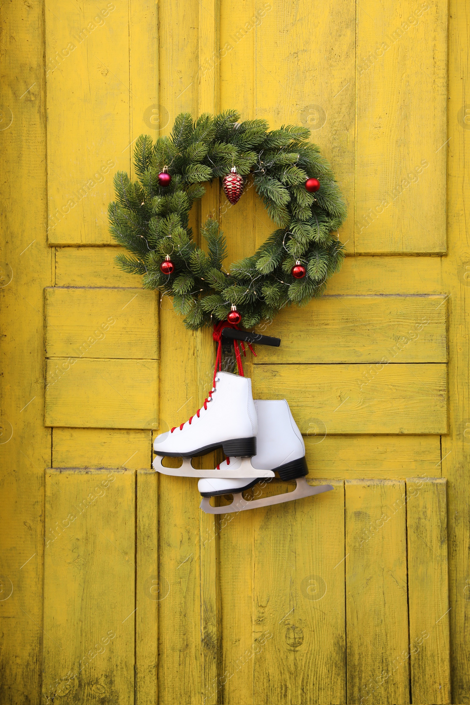 Photo of Pair of ice skates and Christmas wreath hanging on old yellow door