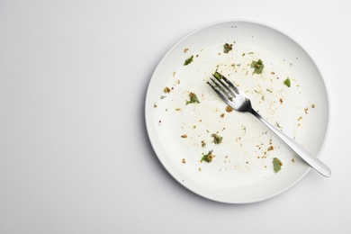 Photo of Dirty plate with food leftovers and fork on white background, top view