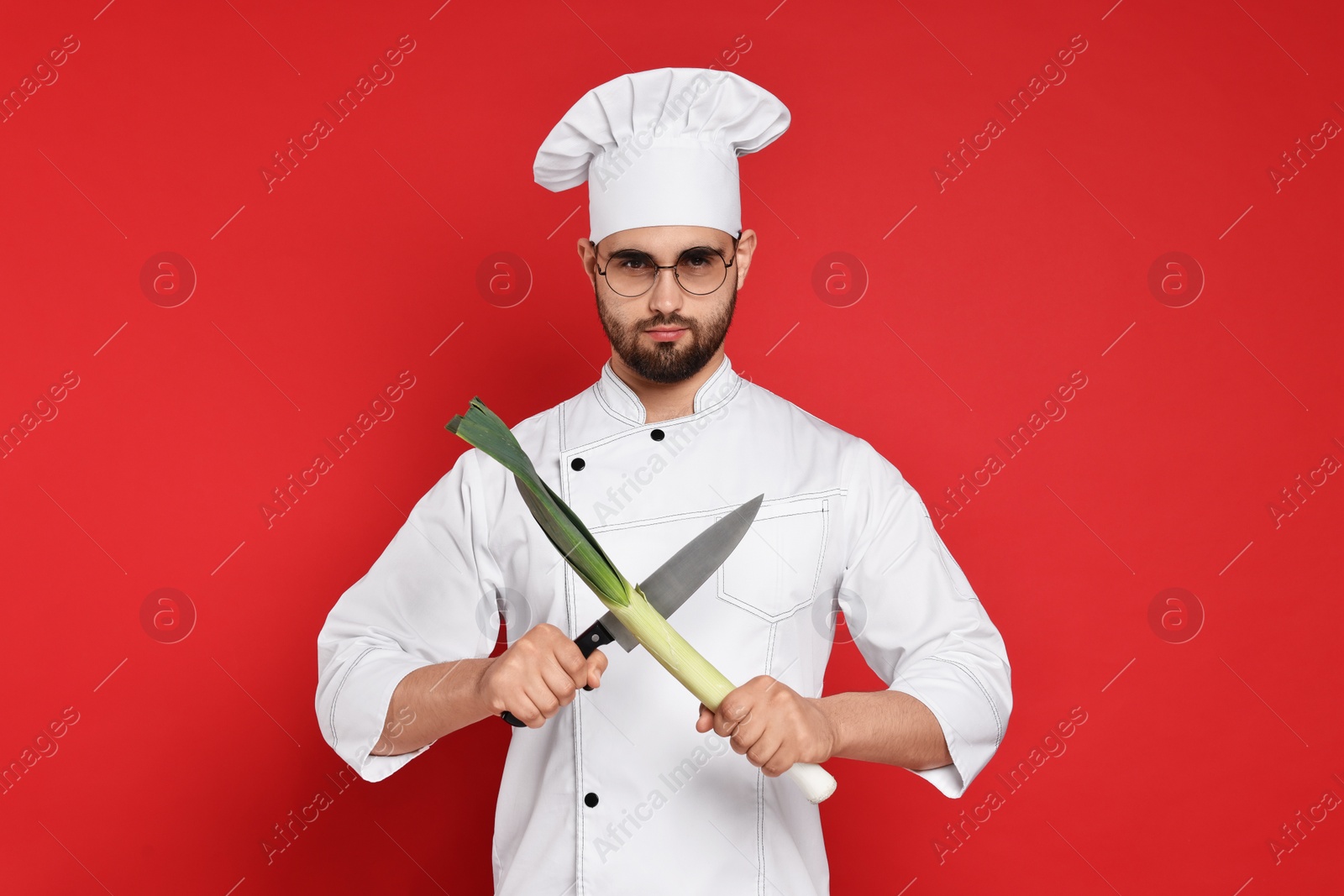 Photo of Professional chef with leek and knife having fun on red background