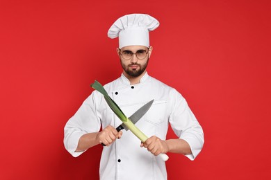 Professional chef with leek and knife having fun on red background