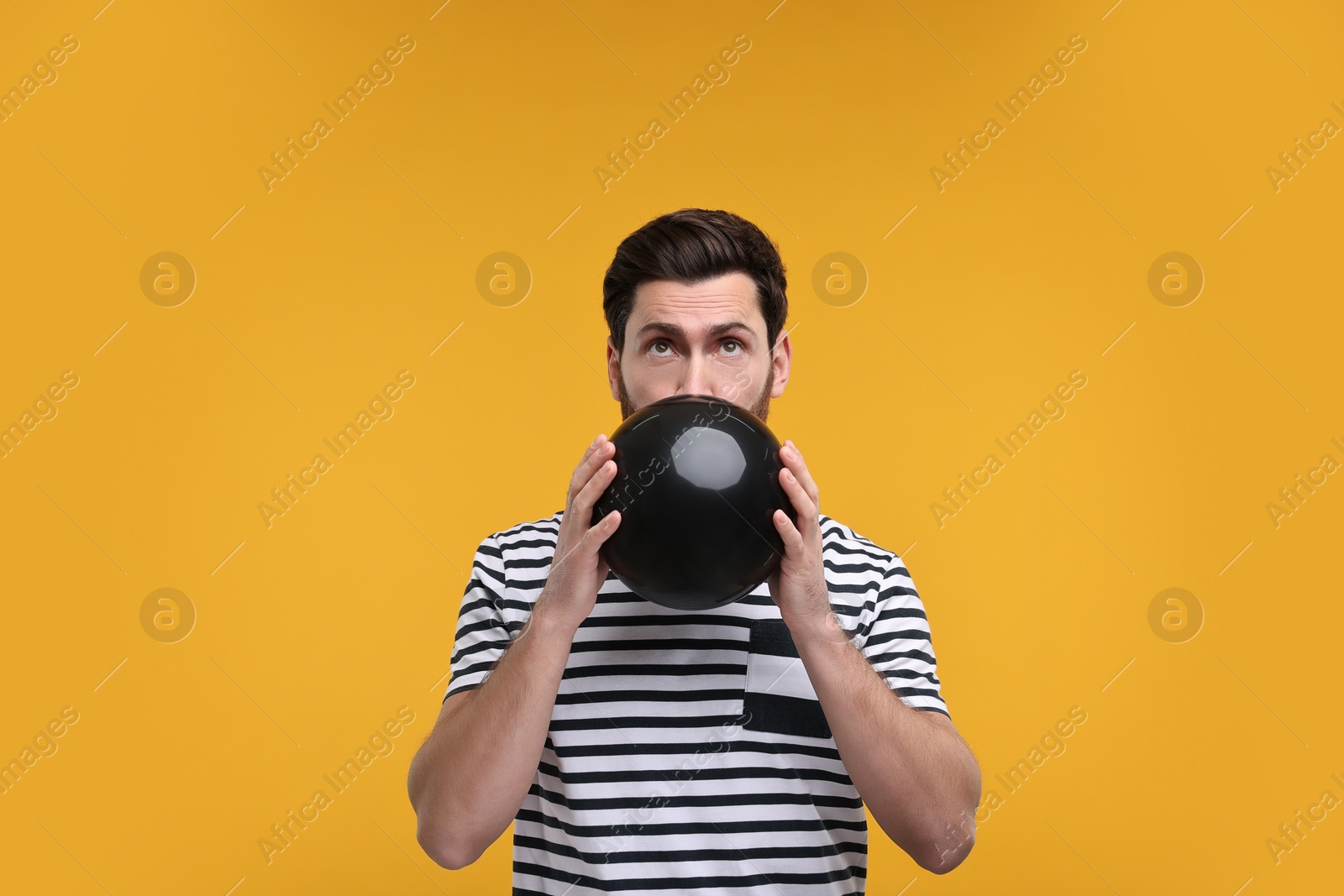 Photo of Man inflating black balloon on yellow background