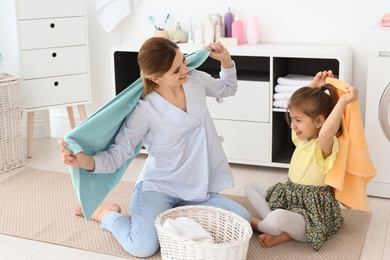 Photo of Housewife with daughter having fun while folding freshly washed towels in laundry room